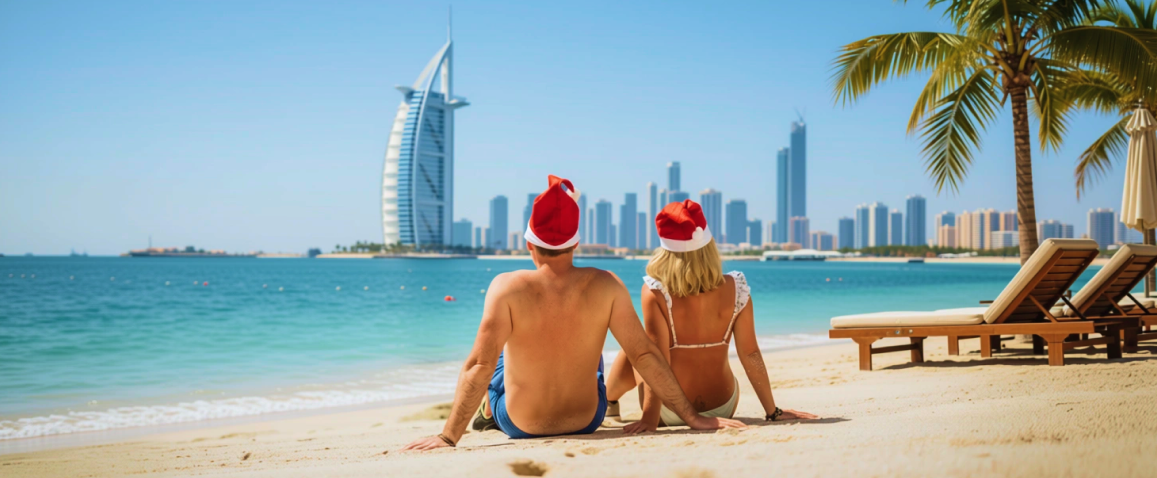 Para na plaży w czapeczkach św. mikołaja z widokiem na Dubaj
